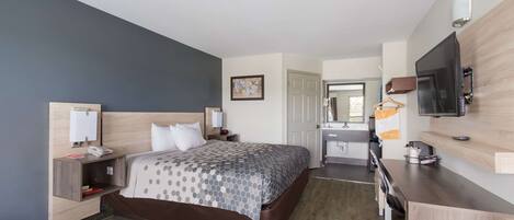 A hotel room with a bed, bedside table, lamp, TV, and a desk with a chair.