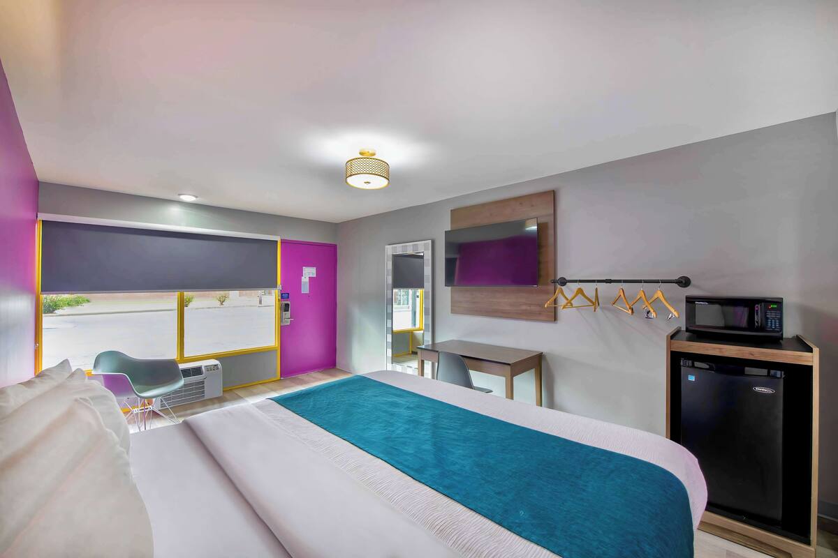 A hotel room with a bed, a desk, a chair, a microwave, and a mini-fridge.