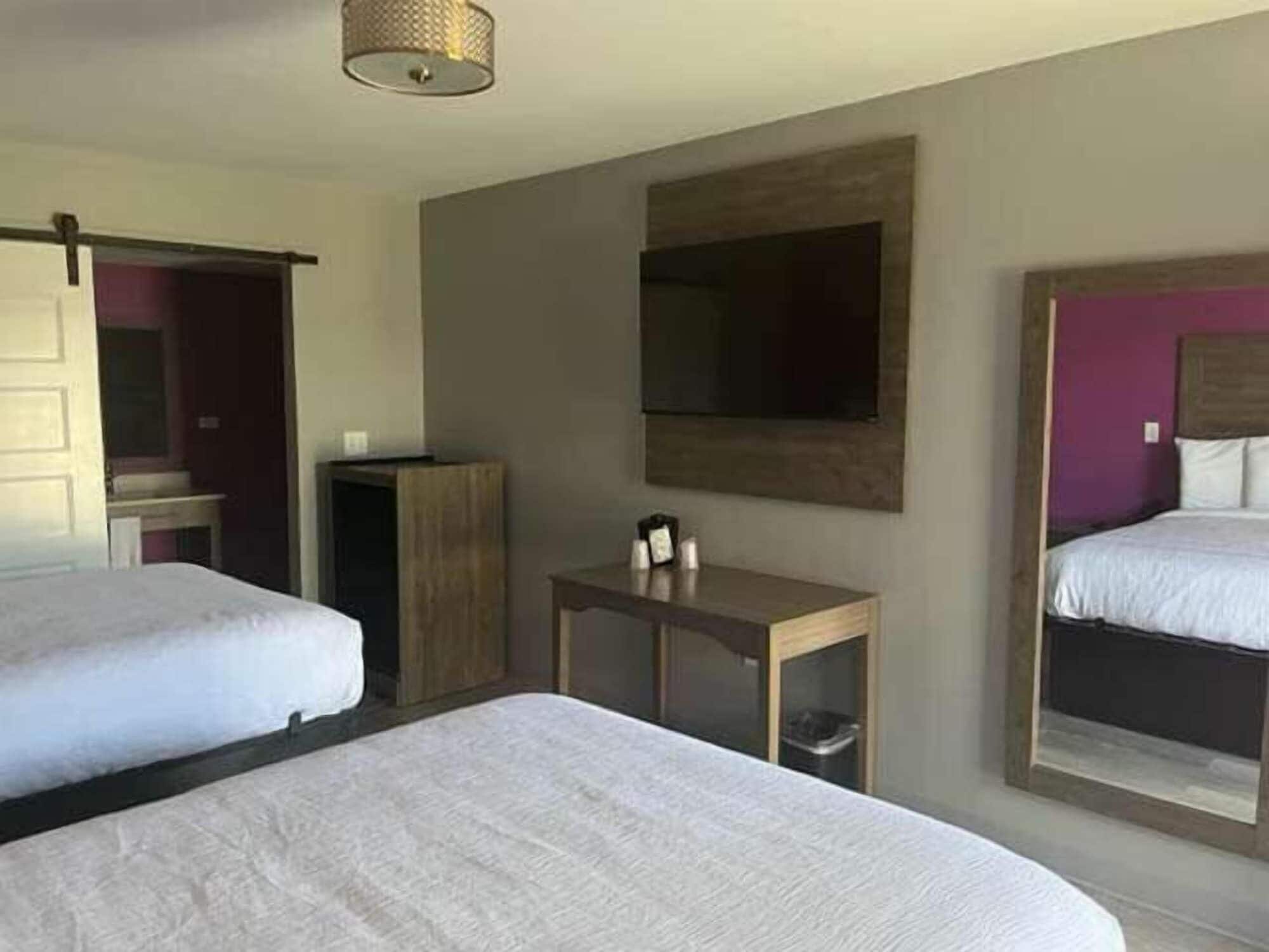 Habitación de hotel con dos camas, una mesita con lámpara, un espejo y televisión en la pared.