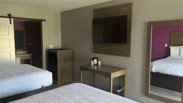 A hotel room with two beds, a small table with a lamp, a mirror, and a television on the wall.