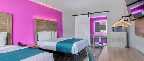 Habitación de hotel moderna con dos camas, un escritorio y un baño visible al fondo.