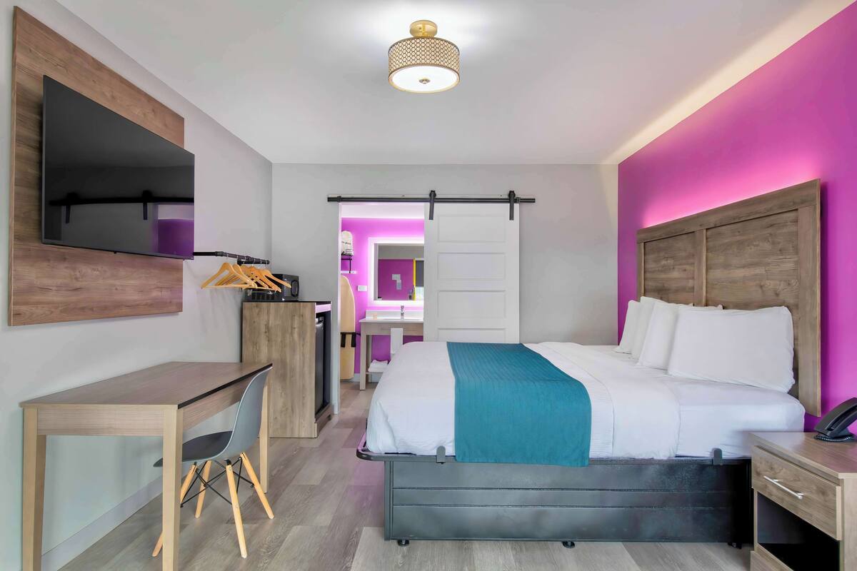 A modern hotel room with a bed, desk, chair, and a TV mounted on the wall.
