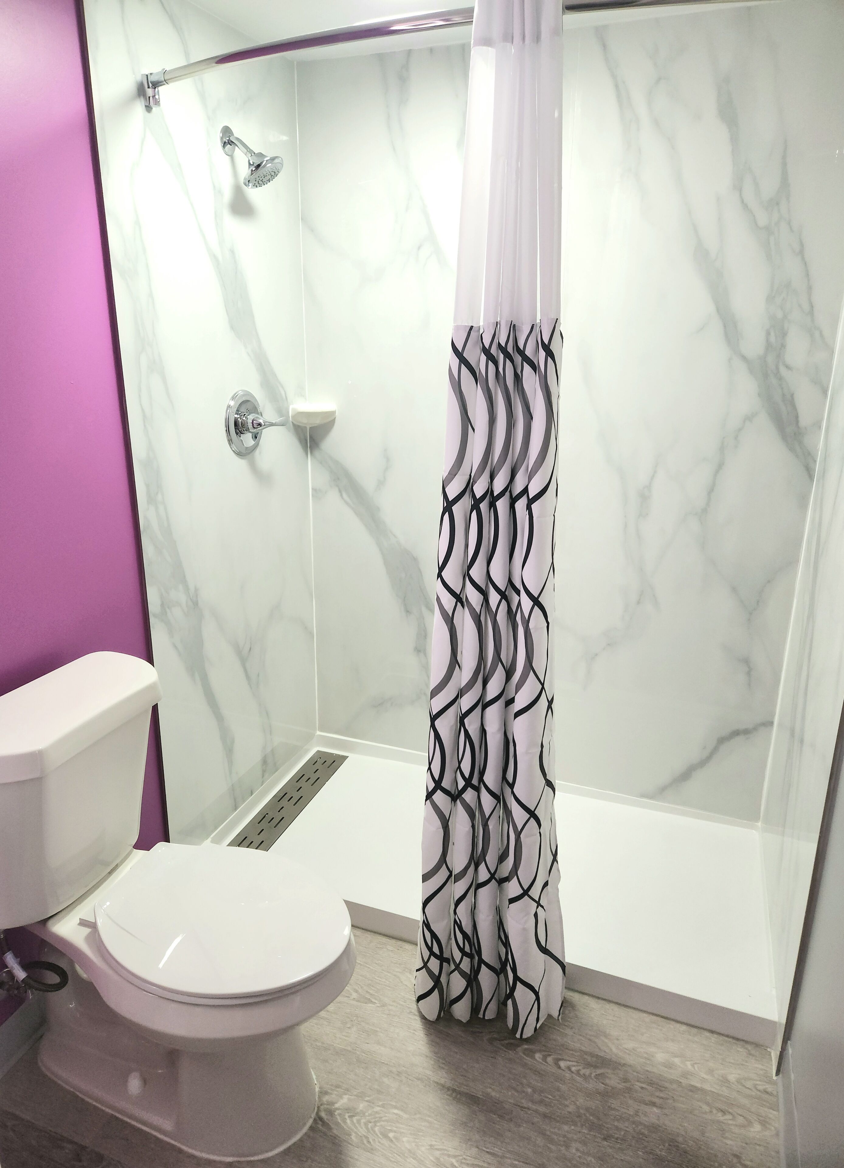 A bathroom with a shower, toilet, and a marble wall.