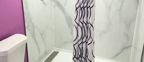 Un baño con ducha, inodoro y pared de mármol.