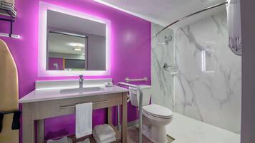 Un baño moderno con pared morada, un espejo grande, un lavabo blanco y una zona de ducha con azulejos de mármol.