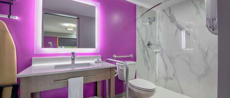 Un baño moderno con pared morada, un espejo grande, un lavabo blanco y una zona de ducha con azulejos de mármol.