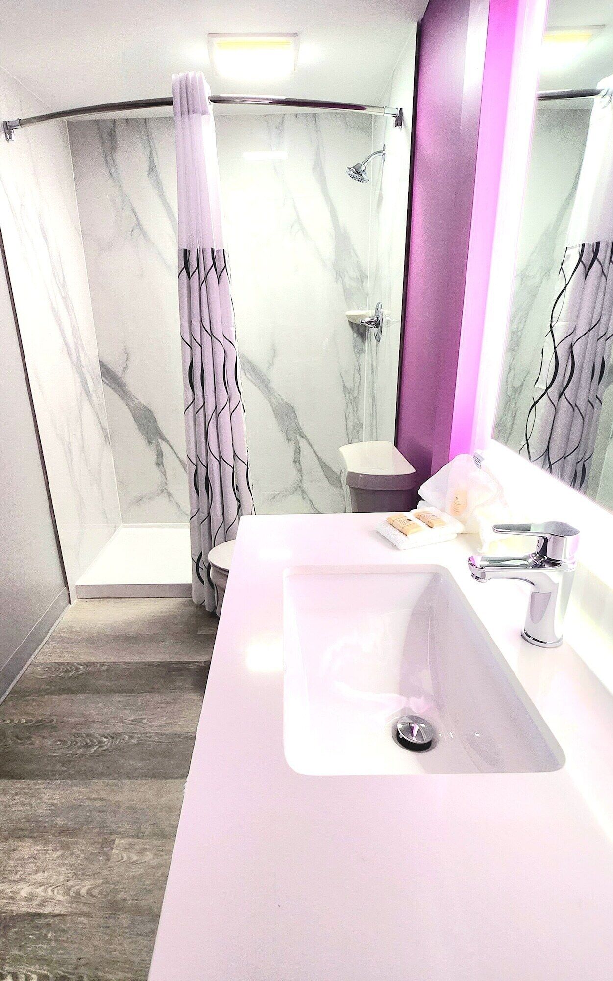 A modern bathroom with a marble shower wall, a white sink, and a vanity mirror.