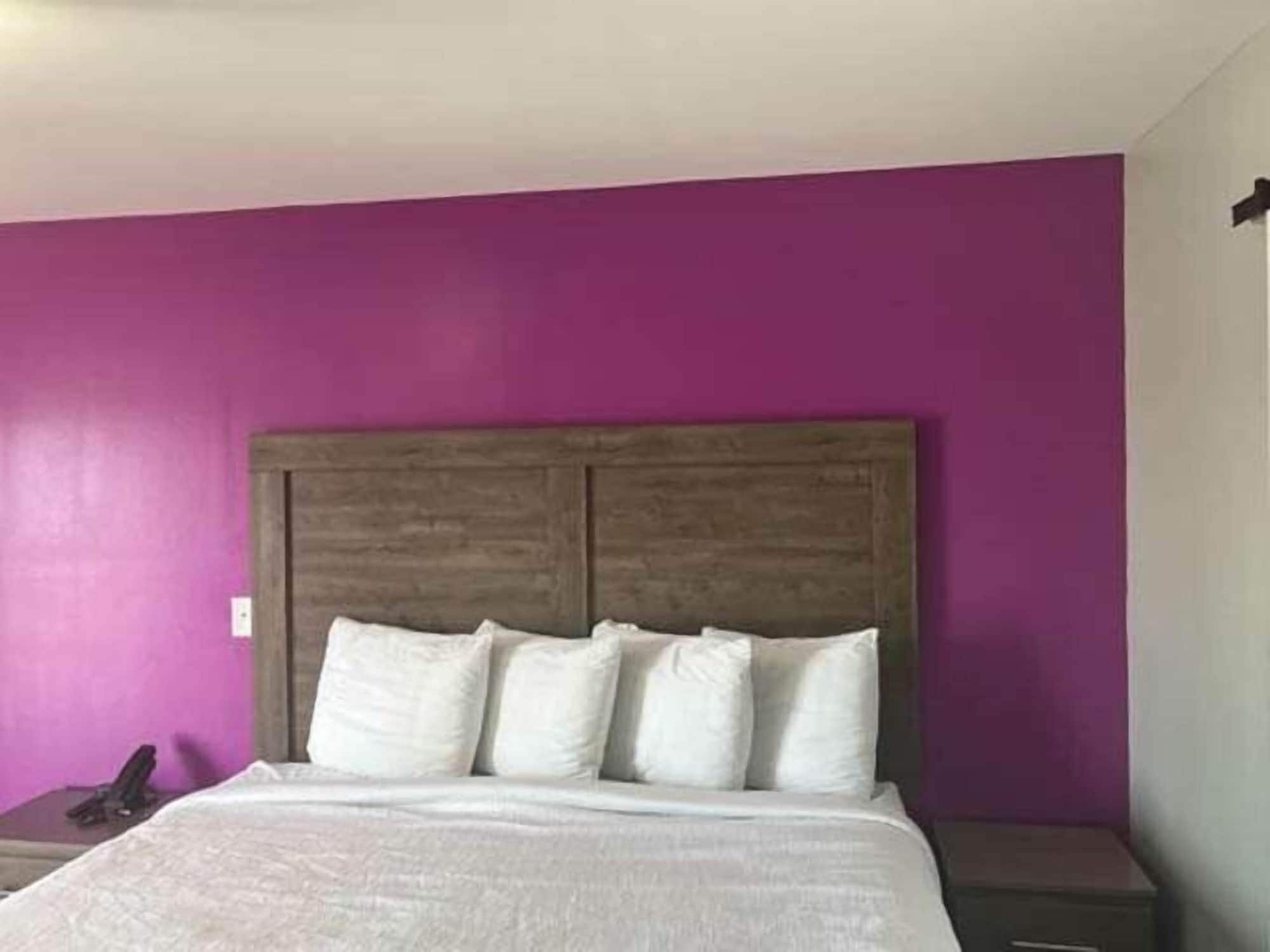 Un dormitorio con cabecera de madera, ropa de cama blanca y pared morada.
