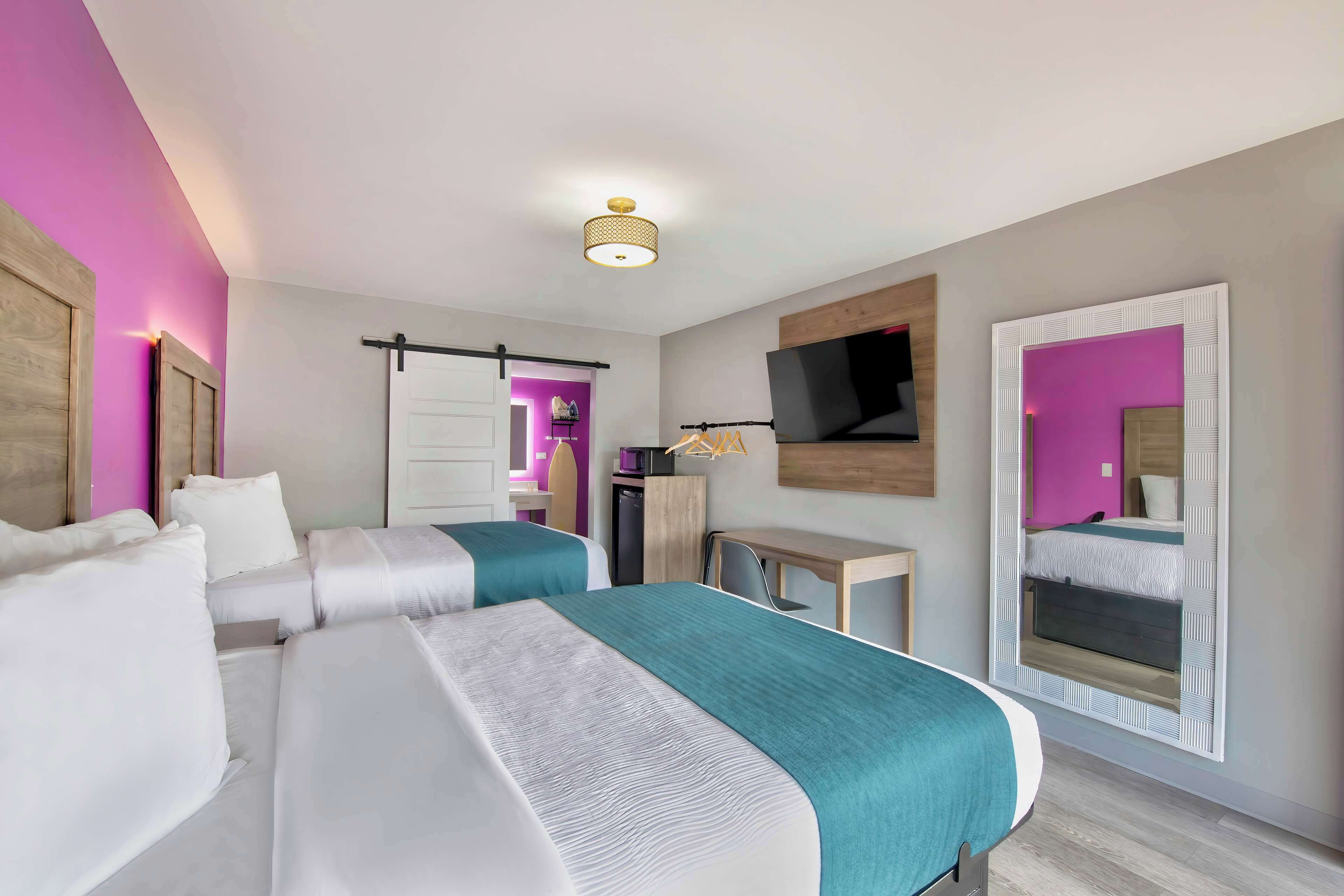 A hotel room with two beds, a TV mounted on the wall, and a small desk.