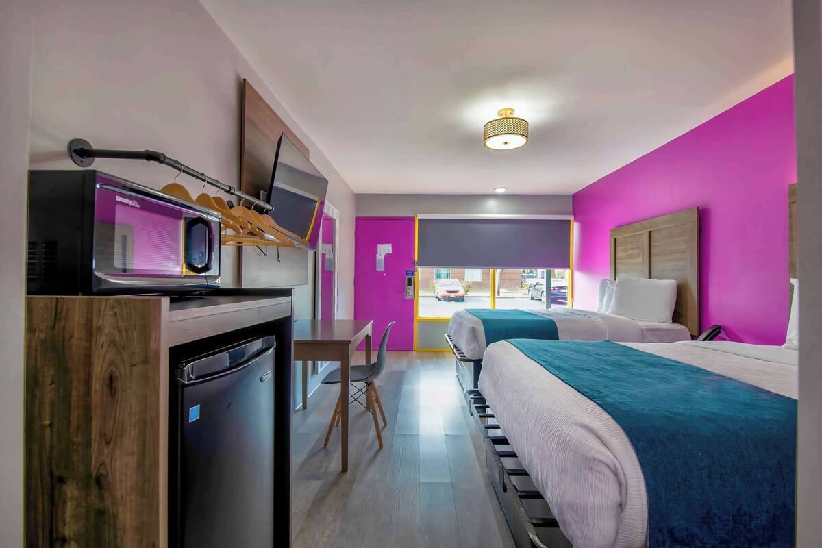 A modern hotel room with a bed, a desk with a computer, a microwave, and a small refrigerator.