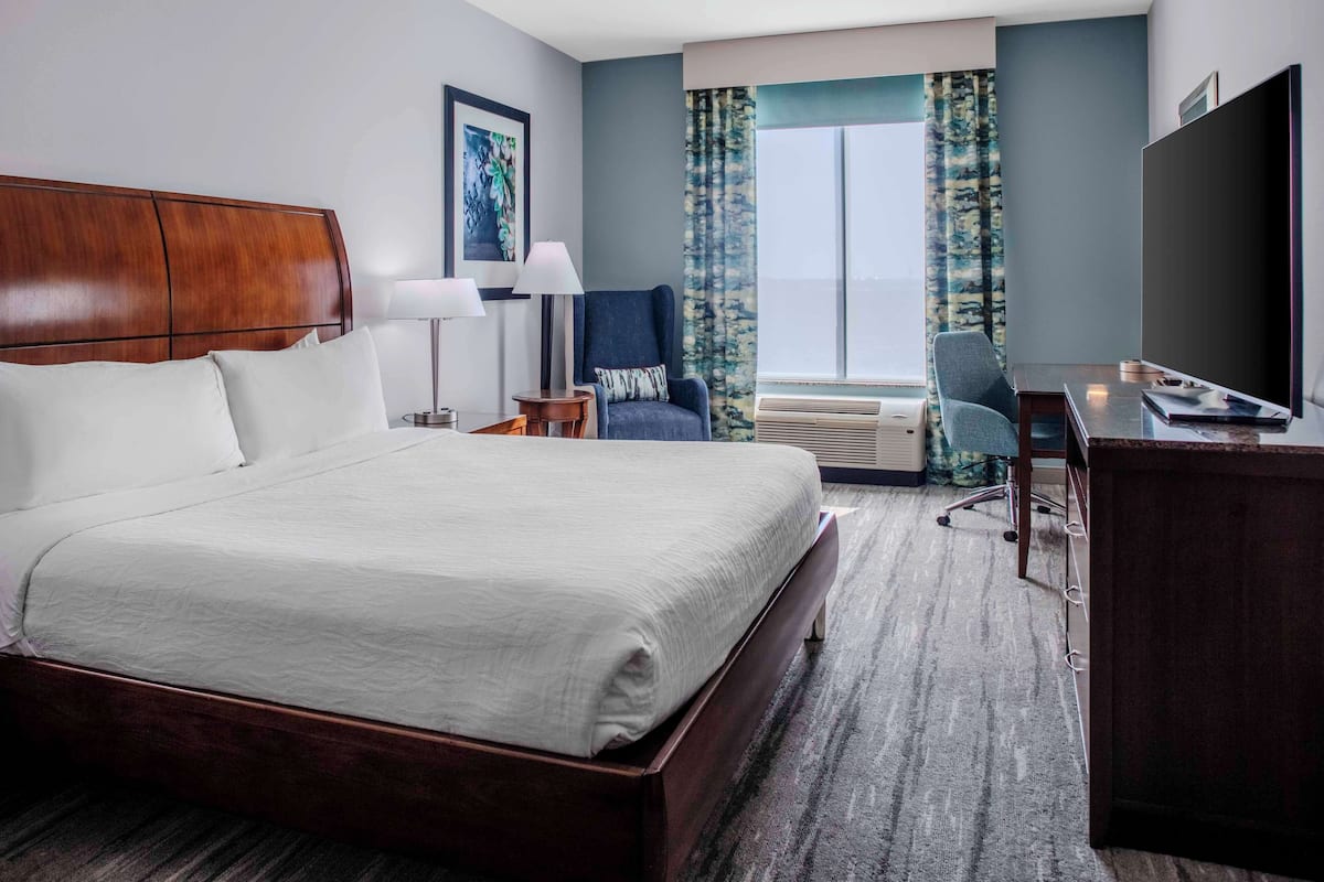 A hotel room with a large bed, a desk, a chair, a TV, and a window with curtains.
