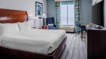 A hotel room with a large bed, a desk, a chair, a TV, and a window with curtains.