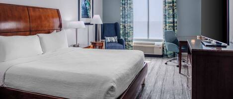 A hotel room with a large bed, a desk, a chair, a TV, and a window with curtains.