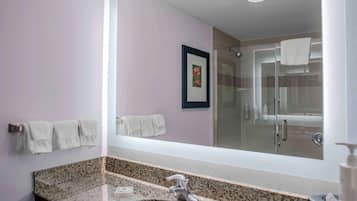 A bathroom with a granite countertop, a sink, a mirror, and a glass shower enclosure.