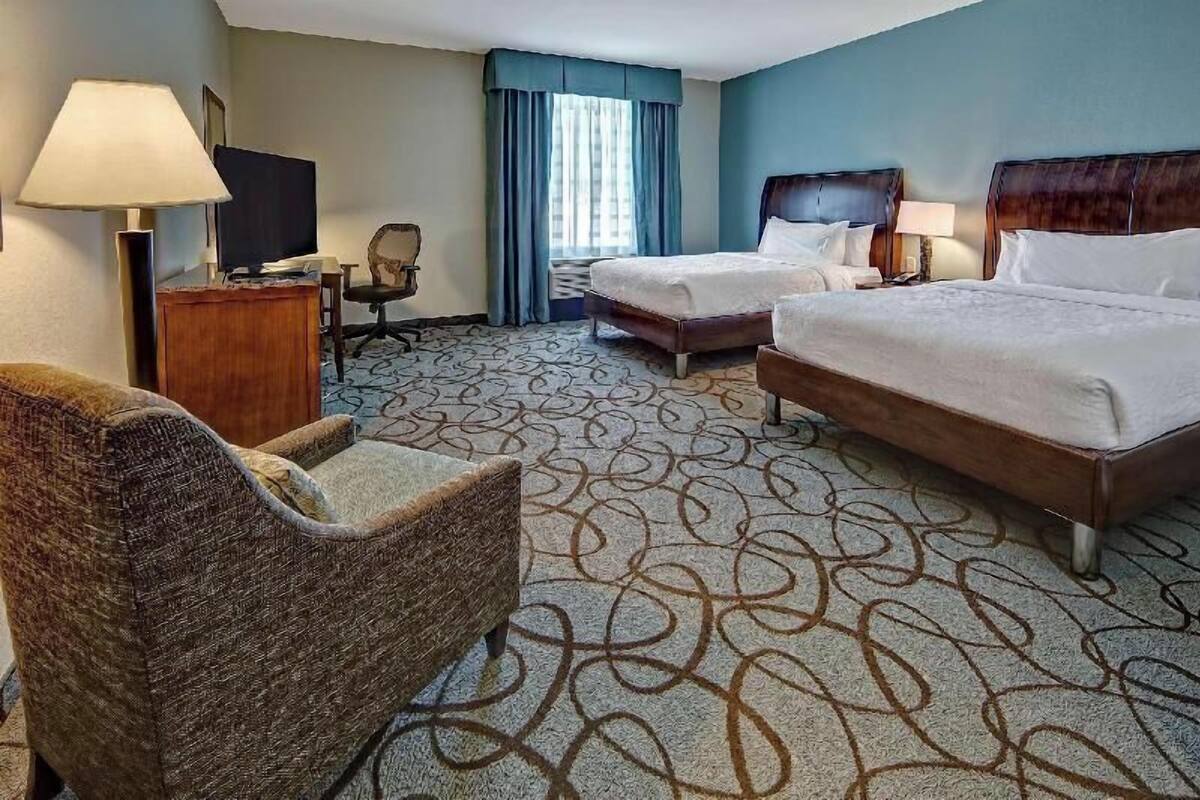 A hotel room with two beds, a desk, a chair, a TV, and a window with curtains.