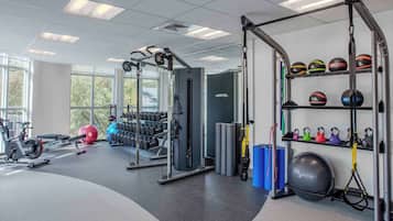 Un gimnasio con equipamiento de ejercicio, kettelbells y mancuernas.