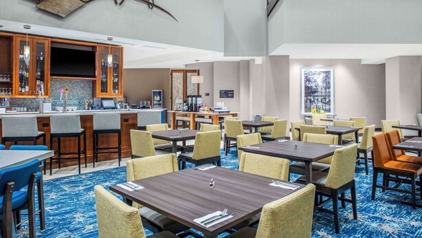 Et hotellobby med barområde, flere spiseborde og stole.