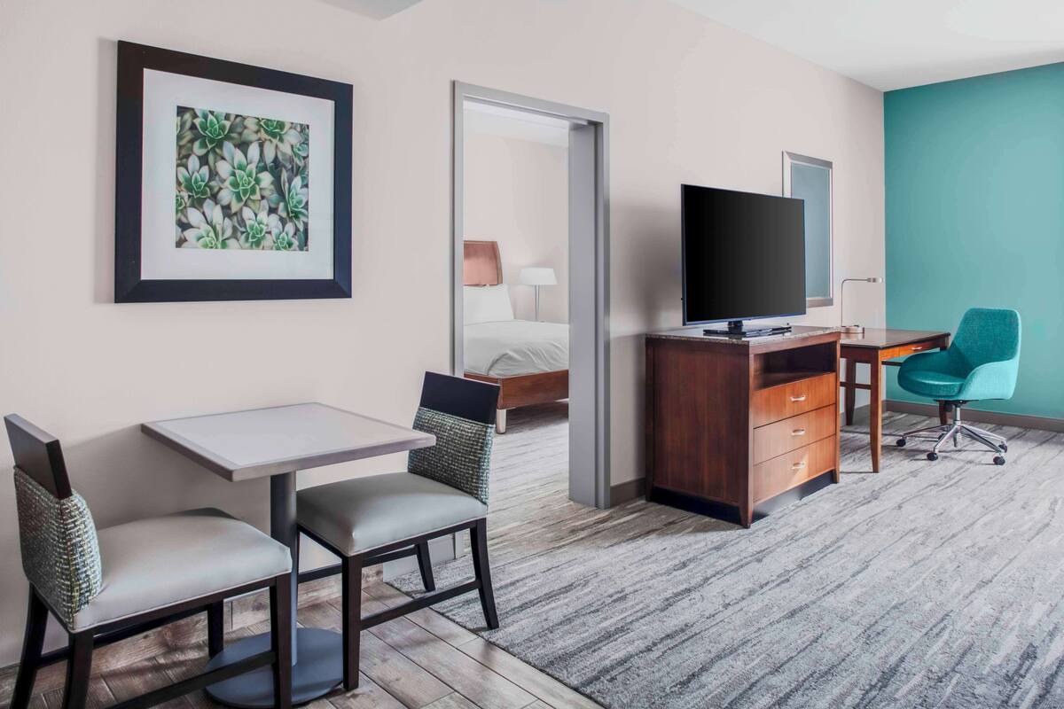 A hotel room with a bed, a desk with a TV, a chair, and a framed picture on the wall.
