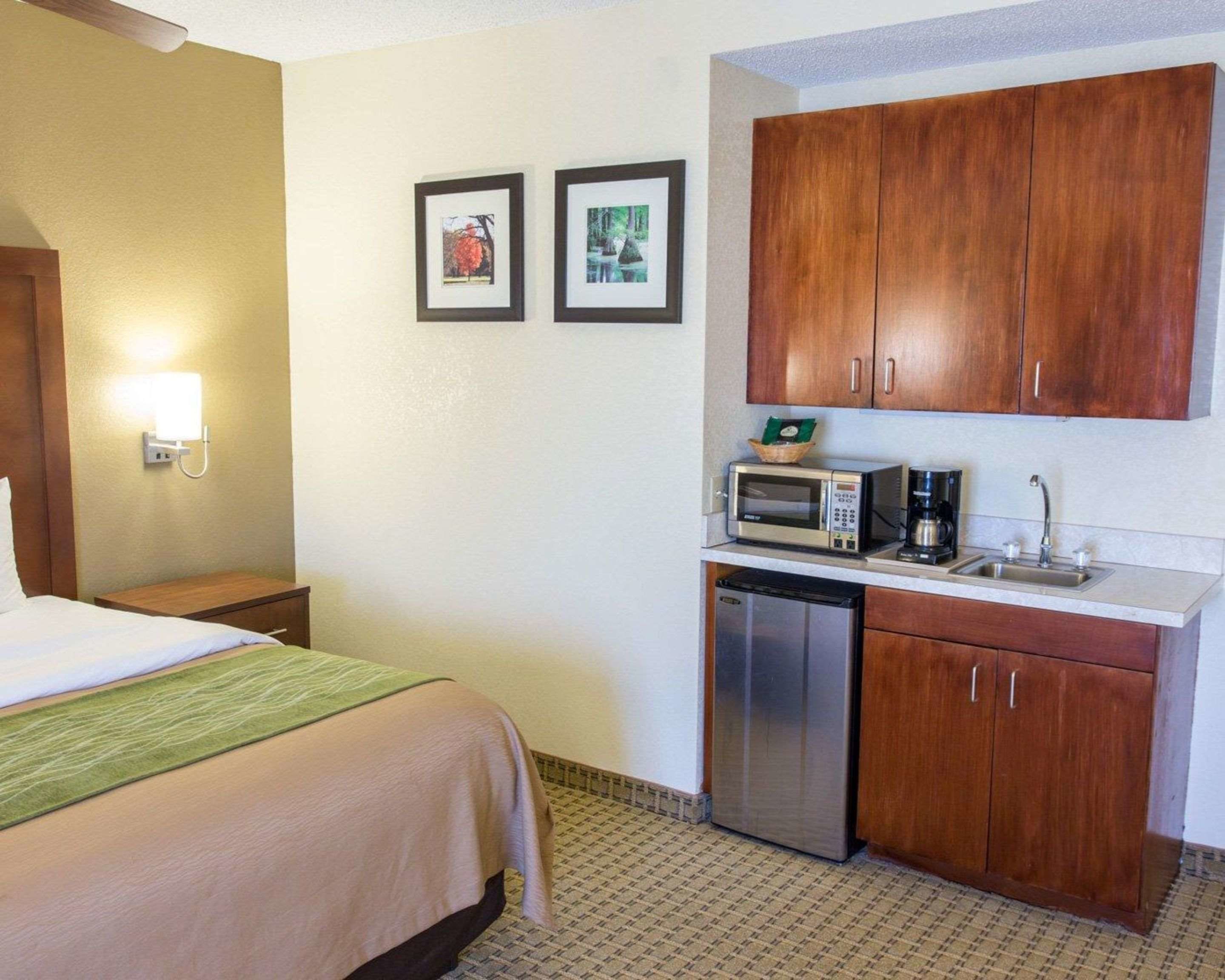 A hotel room with a bed, a small kitchenette with a microwave, coffee maker, and dishwasher, and two framed pictures on the wall.