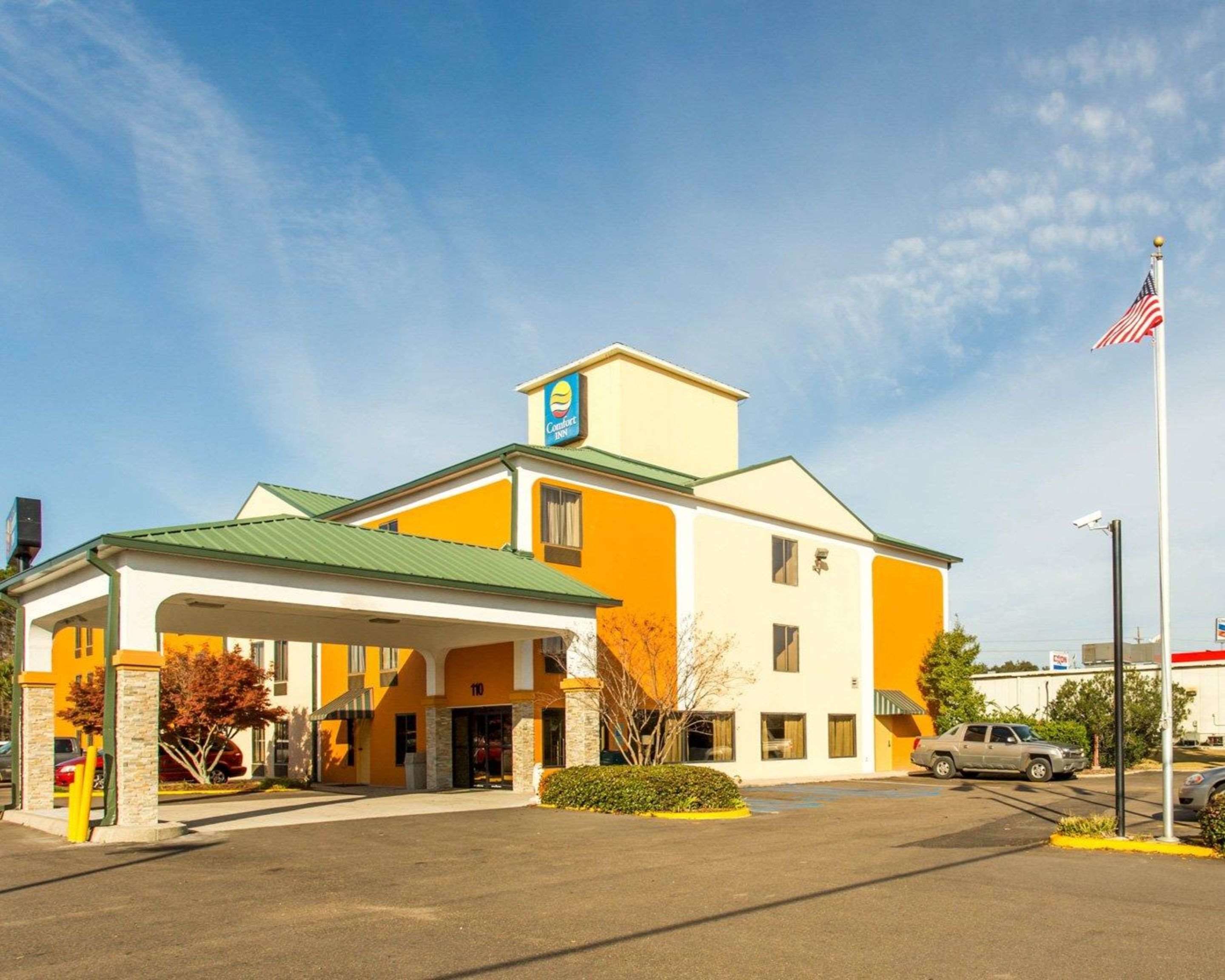 Un hotel Comfort Inn con tetto verde, parcheggio e bandiera americana.