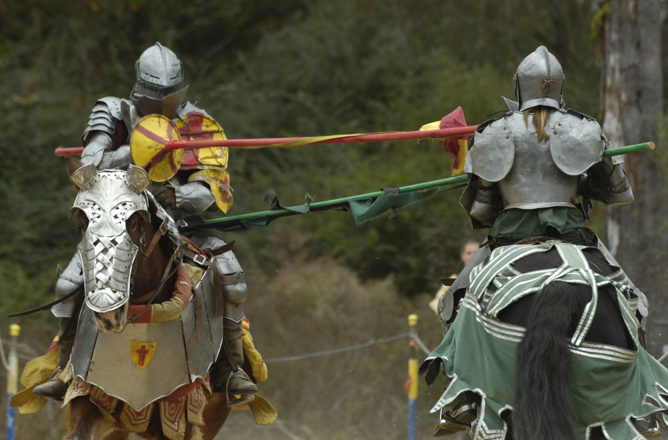 Two individuals in medieval armor on horseback, engaged in a jousting match.