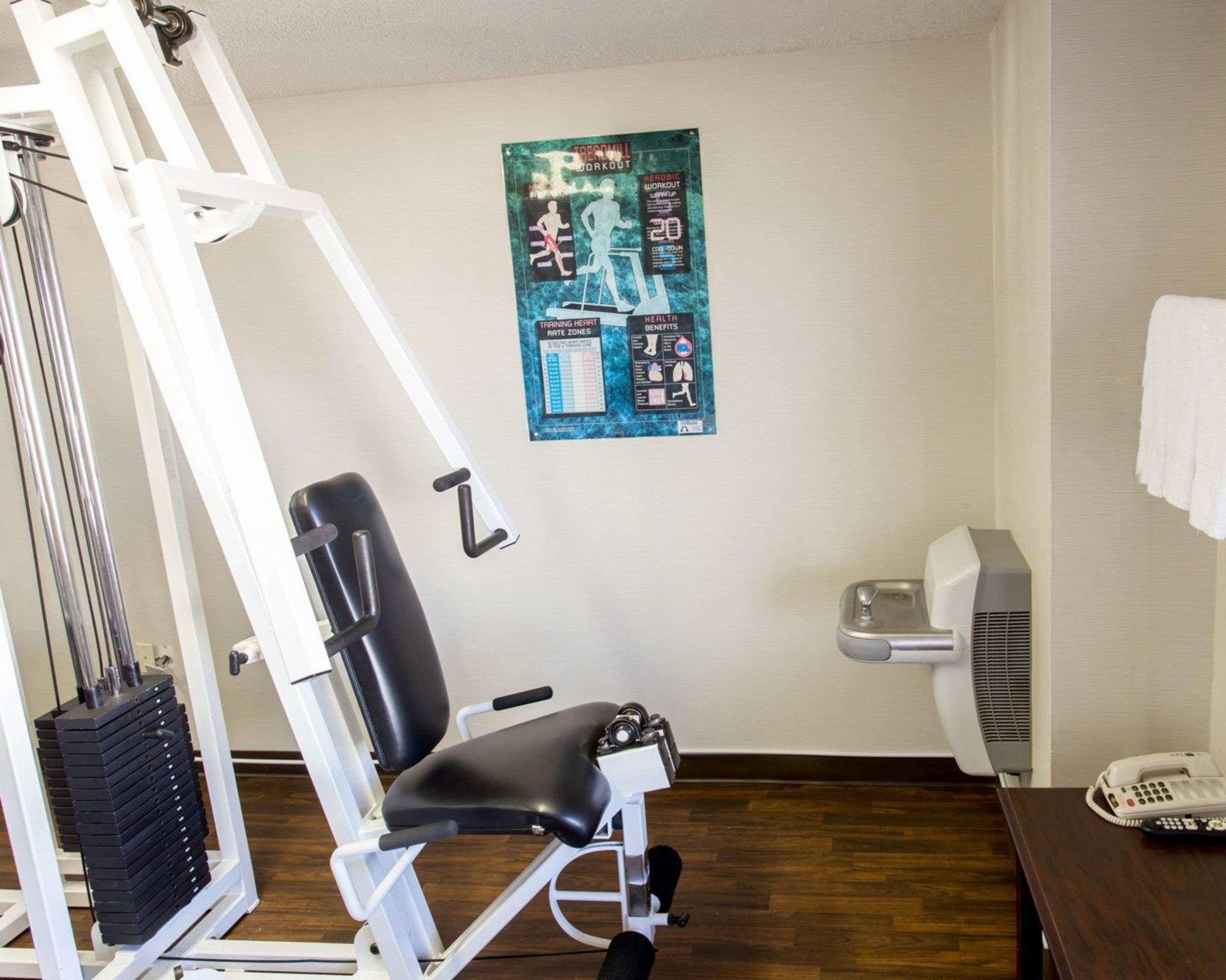 A room with a massage chair, a wall-mounted poster, a white fan, and a telephone on a wooden table.