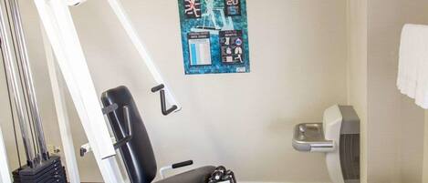 A room with a massage chair, a wall-mounted poster, a white fan, and a telephone on a wooden table.
