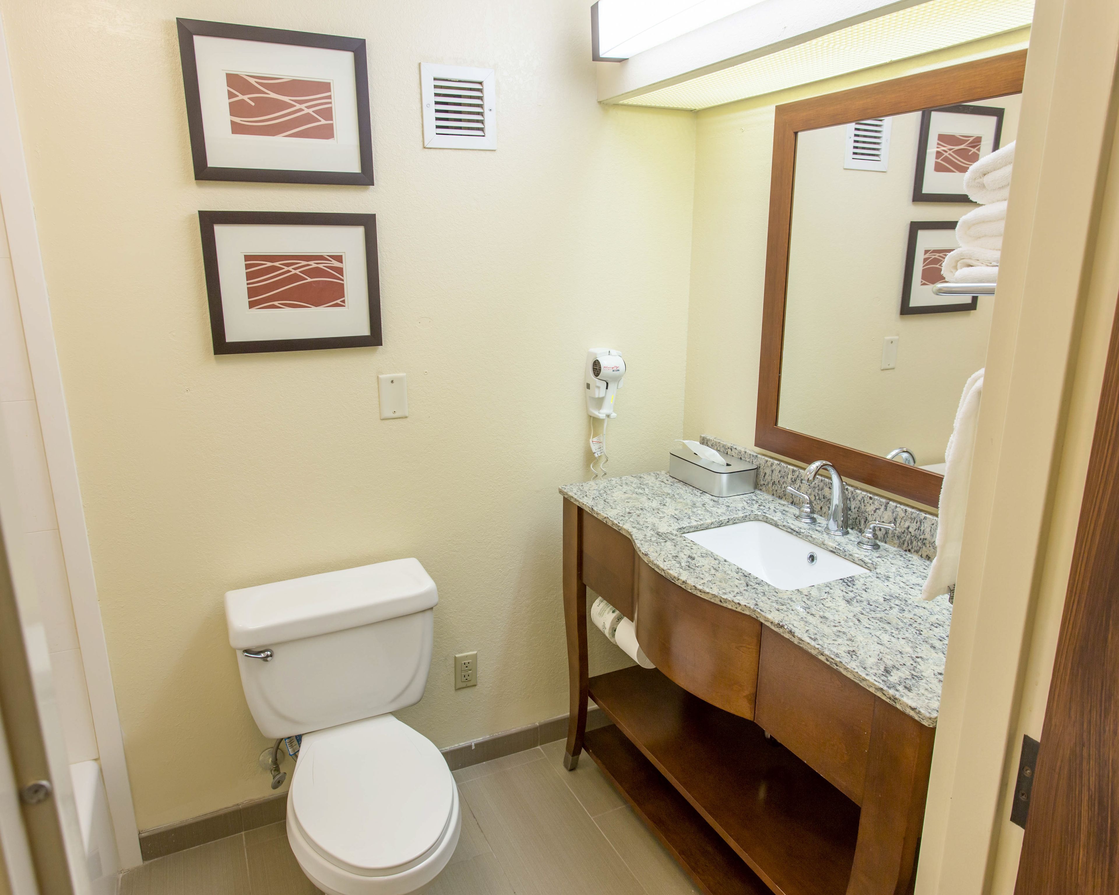 A bathroom with a toilet, sink, and mirror. There are framed pictures on the wall and a towel rack.