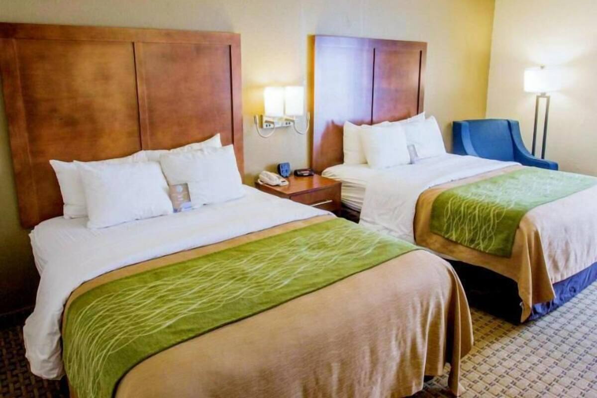 Two double beds with headboards, bedside tables, a lamp, and a chair in a hotel room.