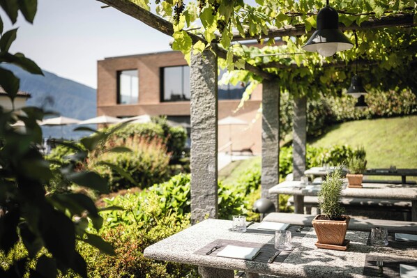 An outdoor dining area with stone tables, potted plants, and hanging lights. - Hotel Belvedere Locarno (Locarno)