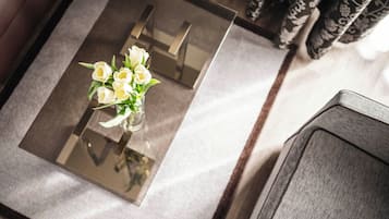 A glass-top table with a bouquet of white flowers, a chair, and patterned curtains in the background.