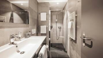 A modern bathroom with a large mirror, a white sink, a shower with a glass door, and a towel rack.
