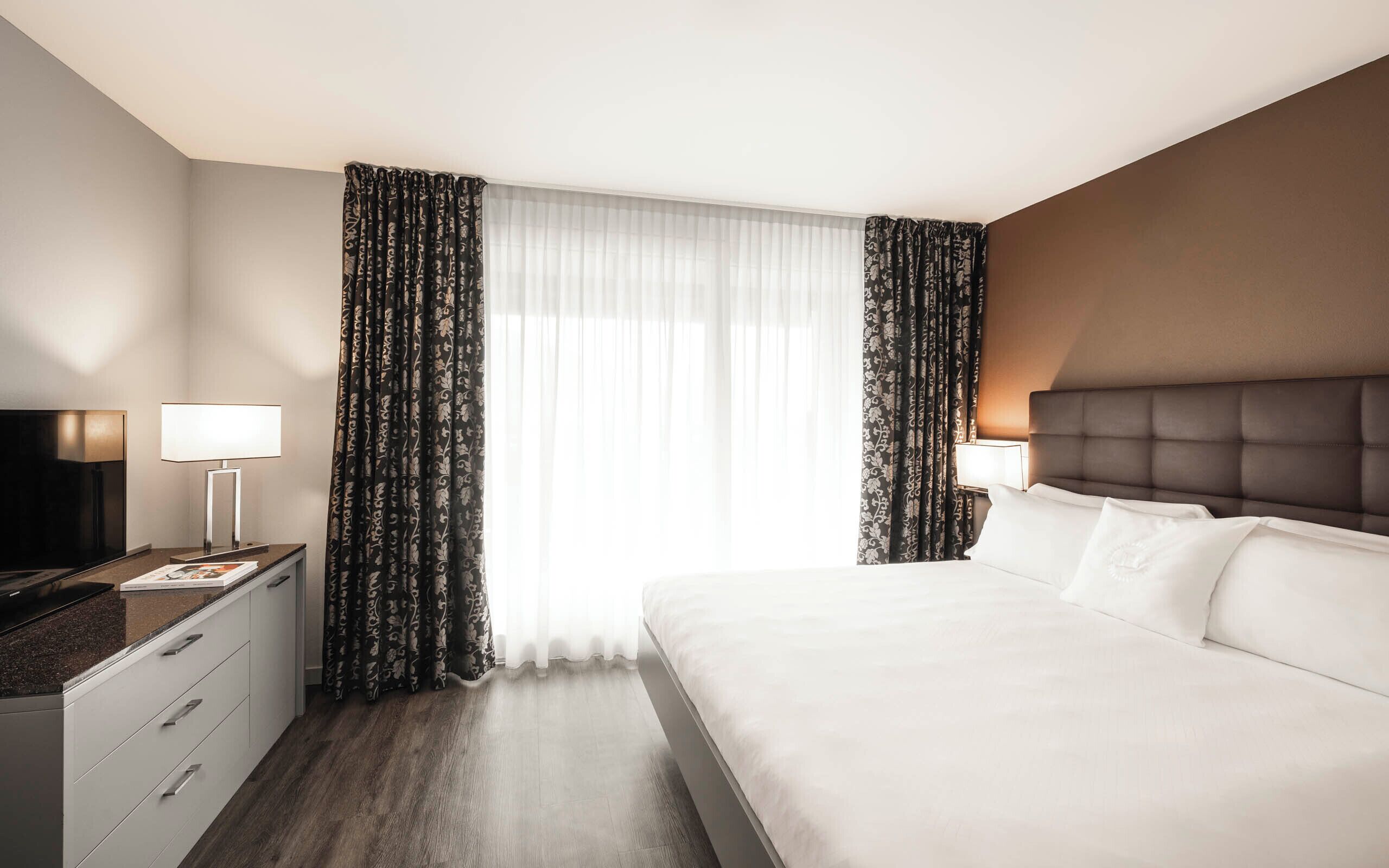 Ett hotellrum med en stor säng, två sängbord med lampor, en platt-TV och mörkt trägolv.