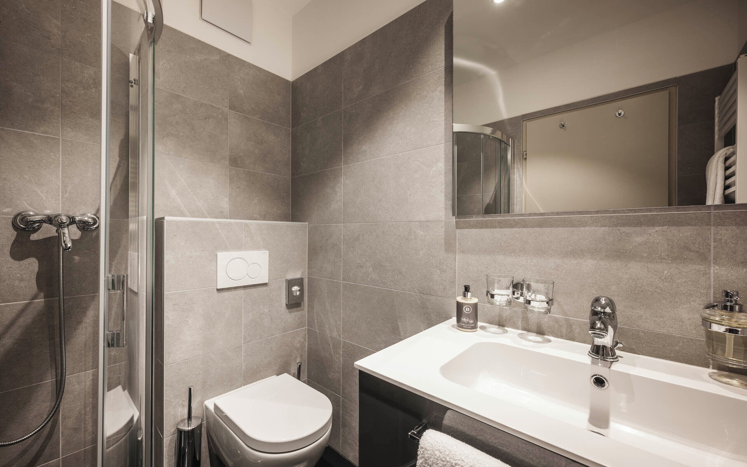 A modern bathroom with a glass-enclosed shower, a white toilet, and a large sink with a mirror above it.