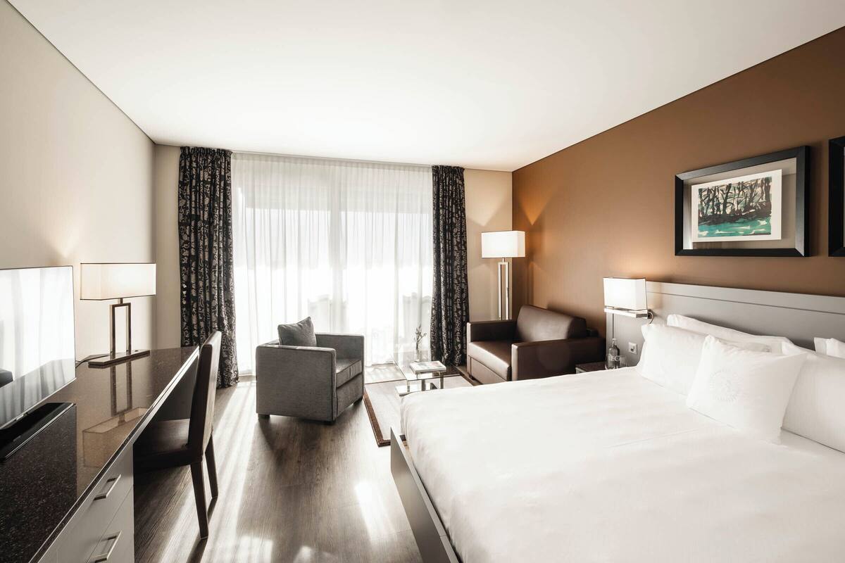 A hotel room with a large bed, a desk, a chair, a sofa, and two lamps.
