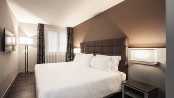 Une chambre d’hôtel avec un grand lit, une table de chevet, un téléviseur à écran plat et une fenêtre avec des rideaux.
