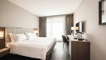 A modern hotel room with a large bed, a desk, a chair, and a TV.