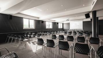 Ein Konferenzraum mit Reihen von Stühlen, einer Projektionsleinwand und großen Fenstern.