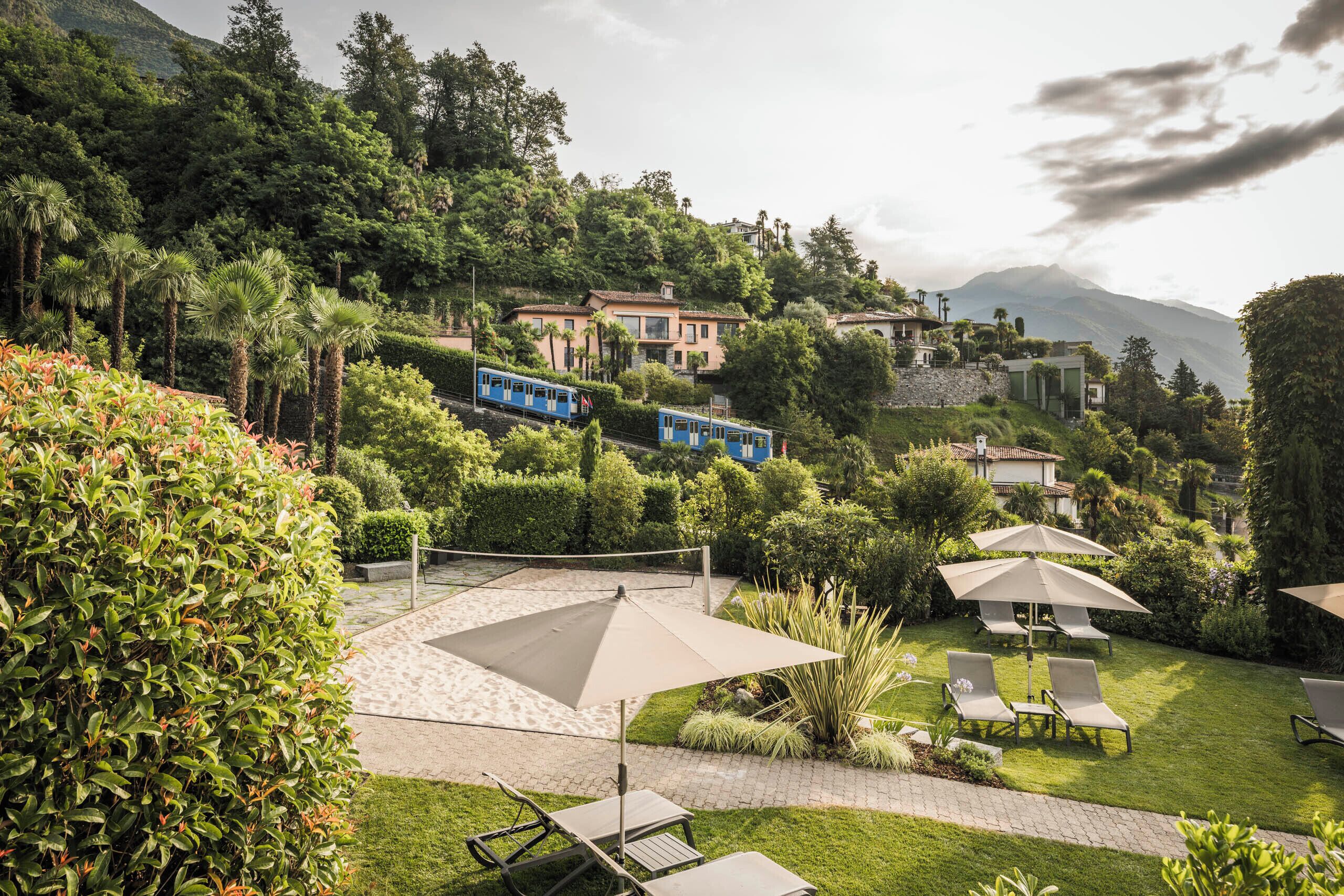 A lush garden with a patio area, outdoor seating, and a train in the background.