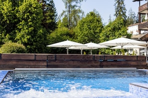 Relax by the serene pool surrounded by lush greenery and a wooden deck.