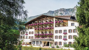A multi-story hotel with balconies adorned with flowers, a well-maintained garden, and a mountainous backdrop.