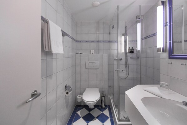 A bathroom with a toilet, sink, shower, and a mirror.