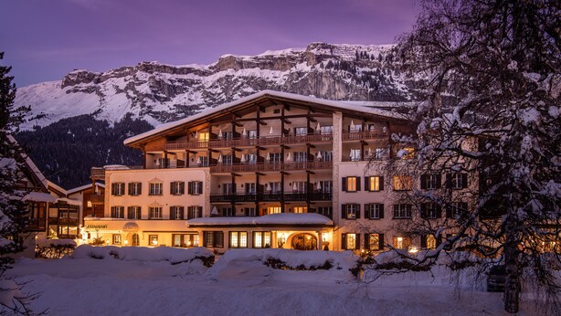 A multi-story hotel with balconies, a restaurant, and a view of snow-covered mountains.
