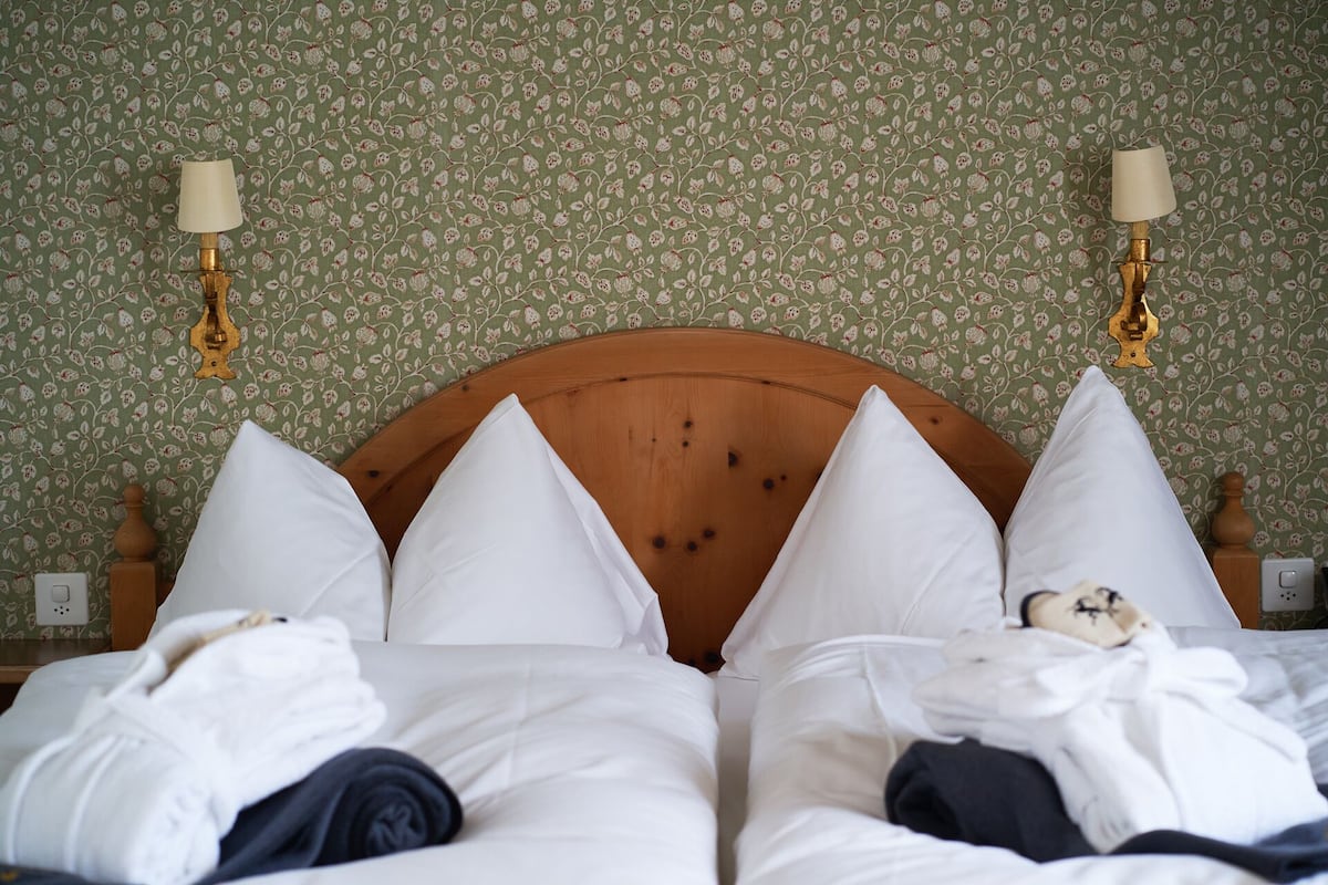 A bed with white bedding, a wooden headboard, and two wall-mounted lamps.