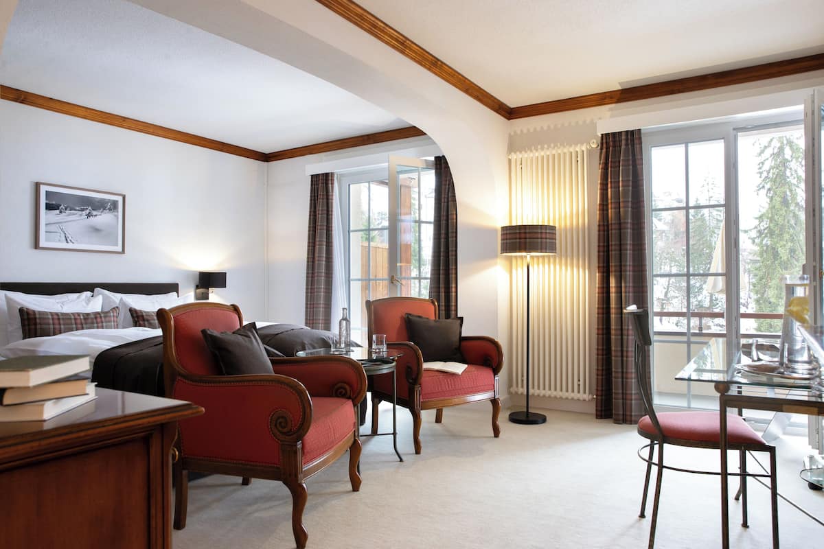 A hotel room with a bed, two armchairs, a table, a lamp, and a window with curtains.