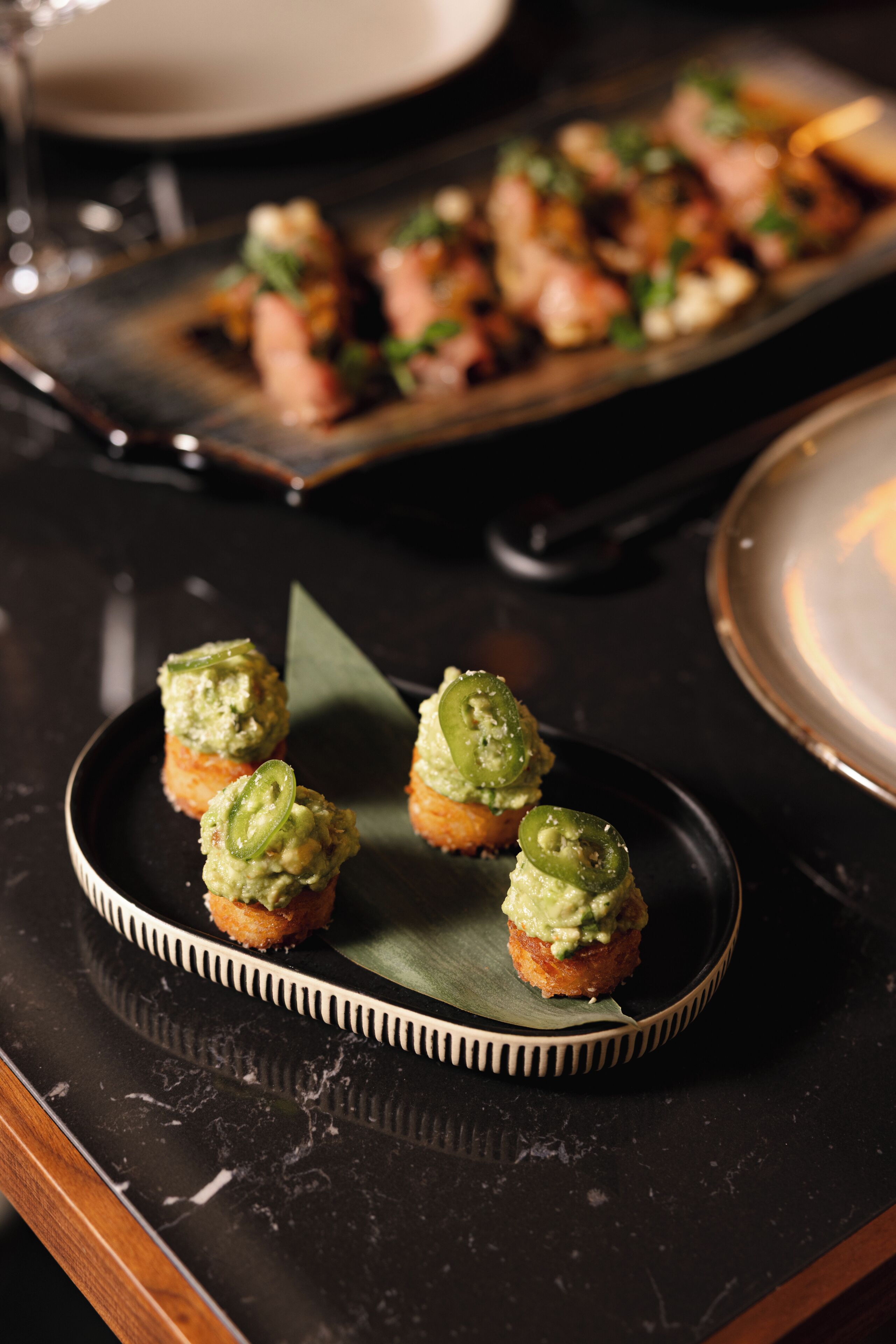 A dessert plate with small pastries topped with green spread and jalapeño slices.