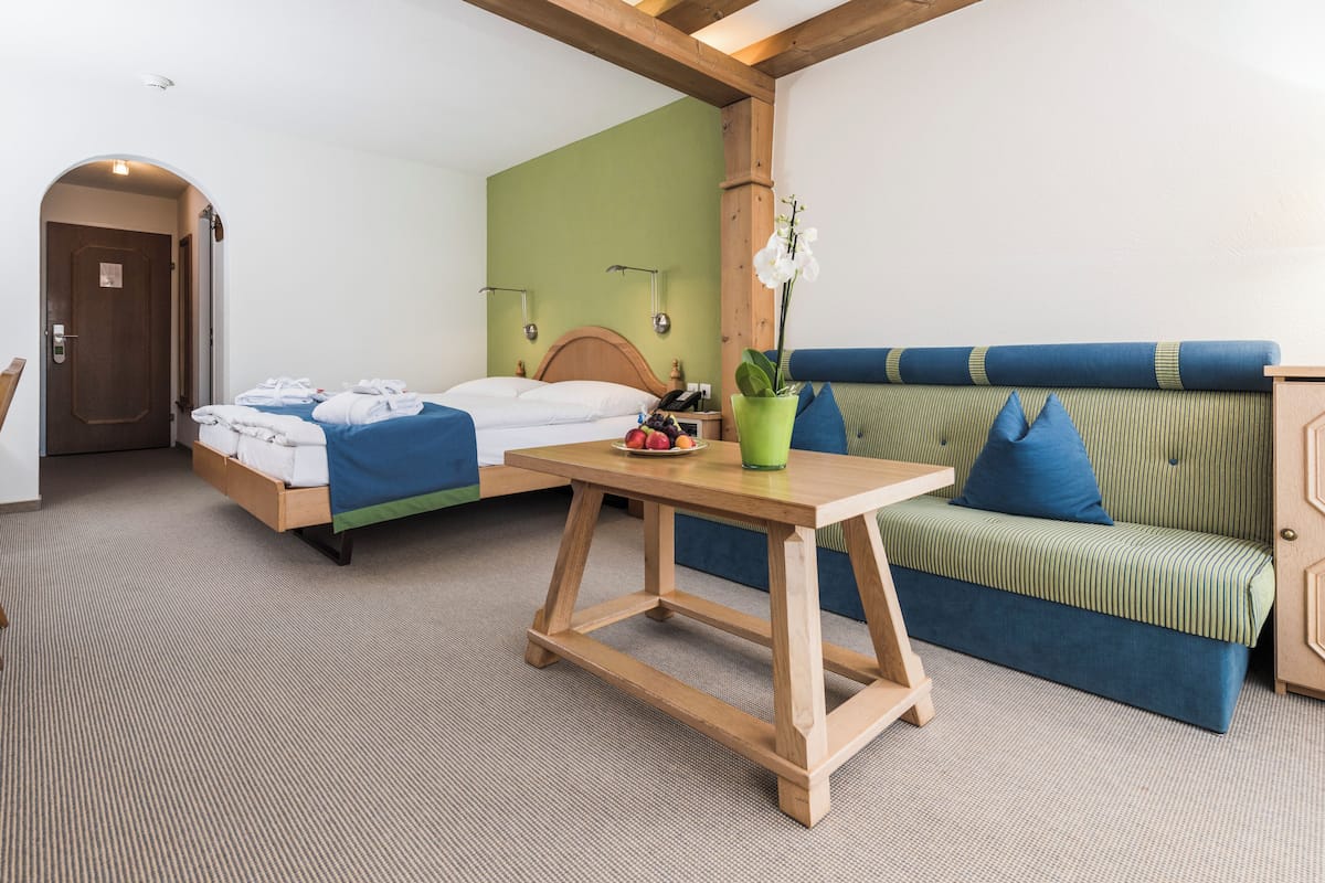 A room with two beds, a wooden table, a green sofa, and a potted orchid.