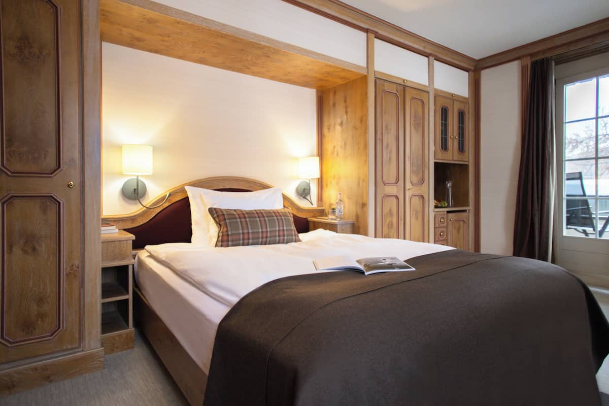 A hotel room with a large bed, wooden headboard, two bedside lamps, a nightstand, and a wardrobe.