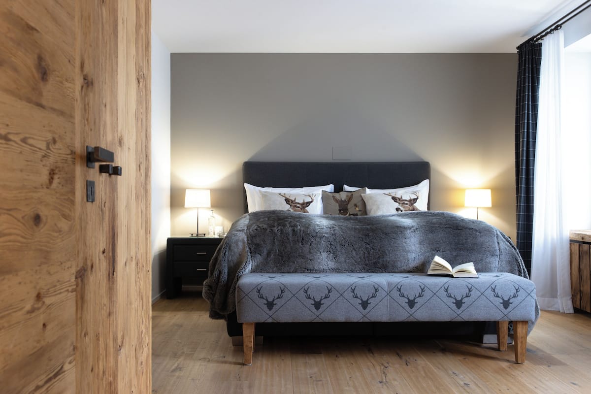 A bedroom with a bed, two bedside lamps, a wooden wardrobe, and a nightstand.