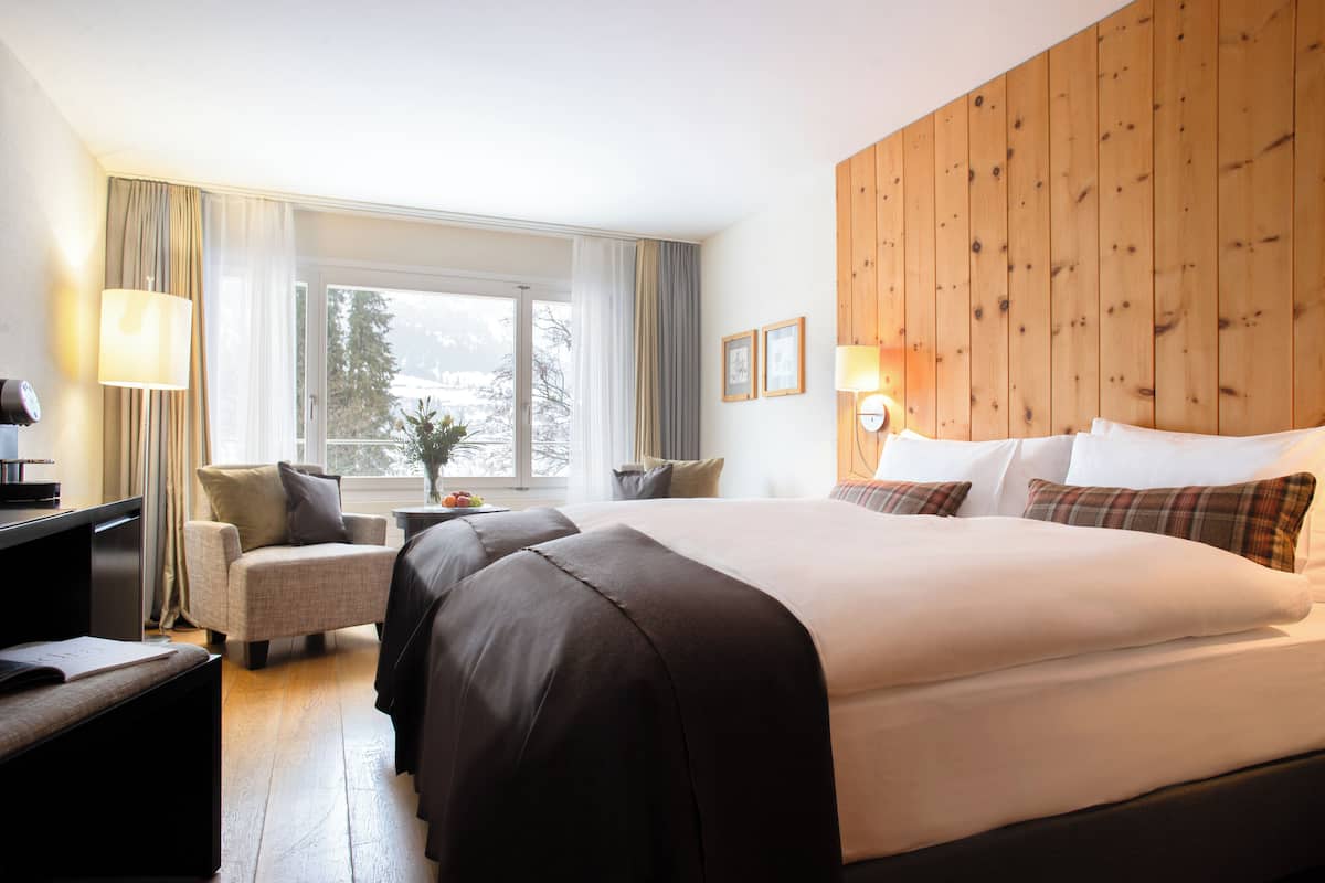 A hotel room with a large bed, a desk, a chair, and a window with curtains.